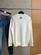 White crewneck sweatshirt with long sleeves and gold logo patch on chest
