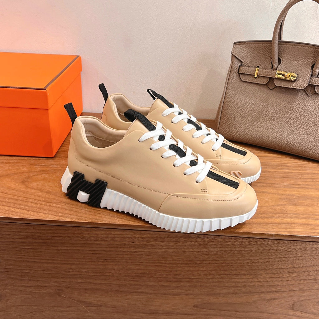 Beige leather low-top sneaker with white laces, black accents, textured tread sole