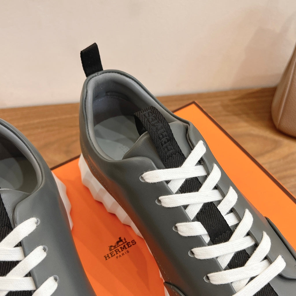 Unisex dark gray sneakers with white laces and Hermes logo on tongue