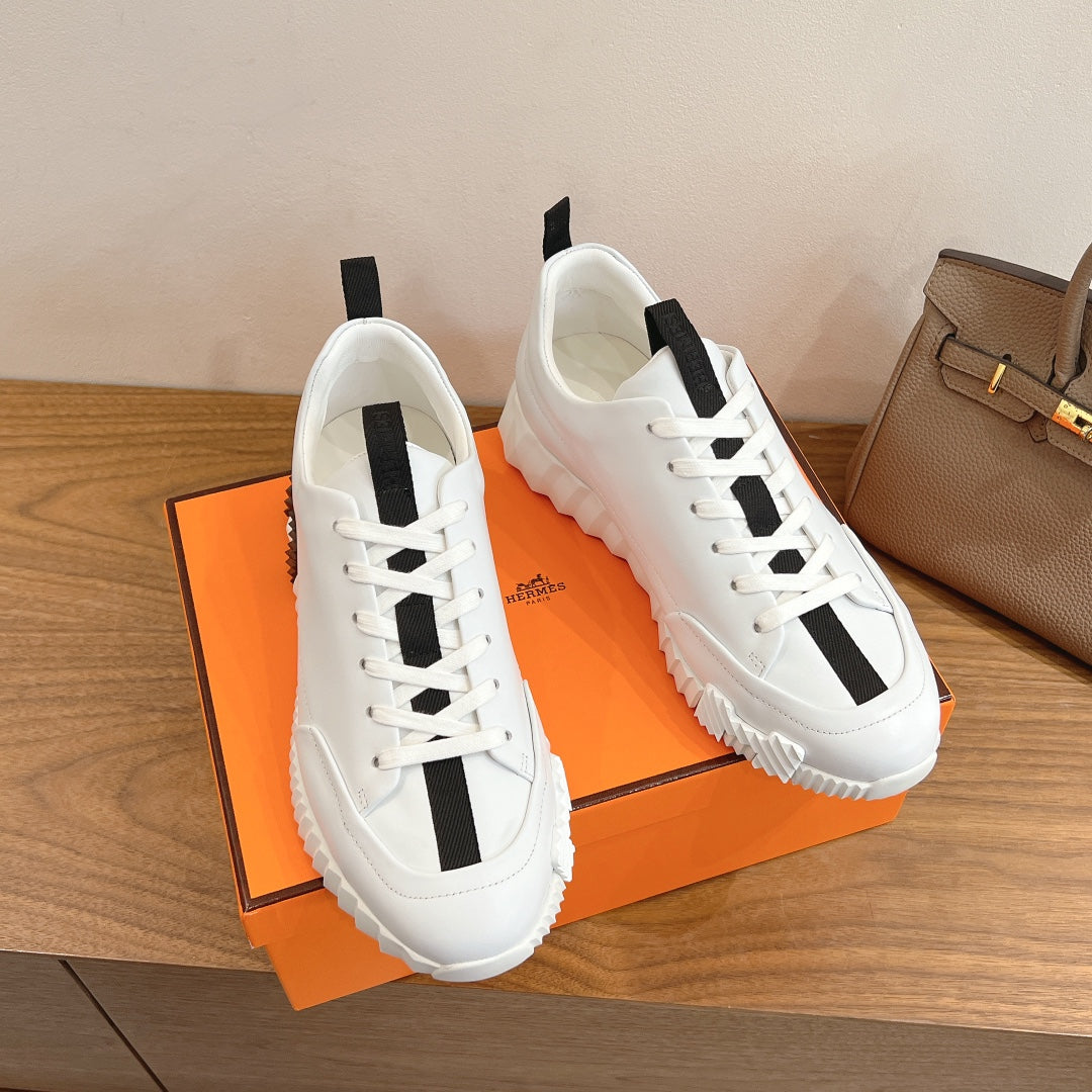 White sneakers on an orange box, black side stripe and thick rubber sole, Hermes.