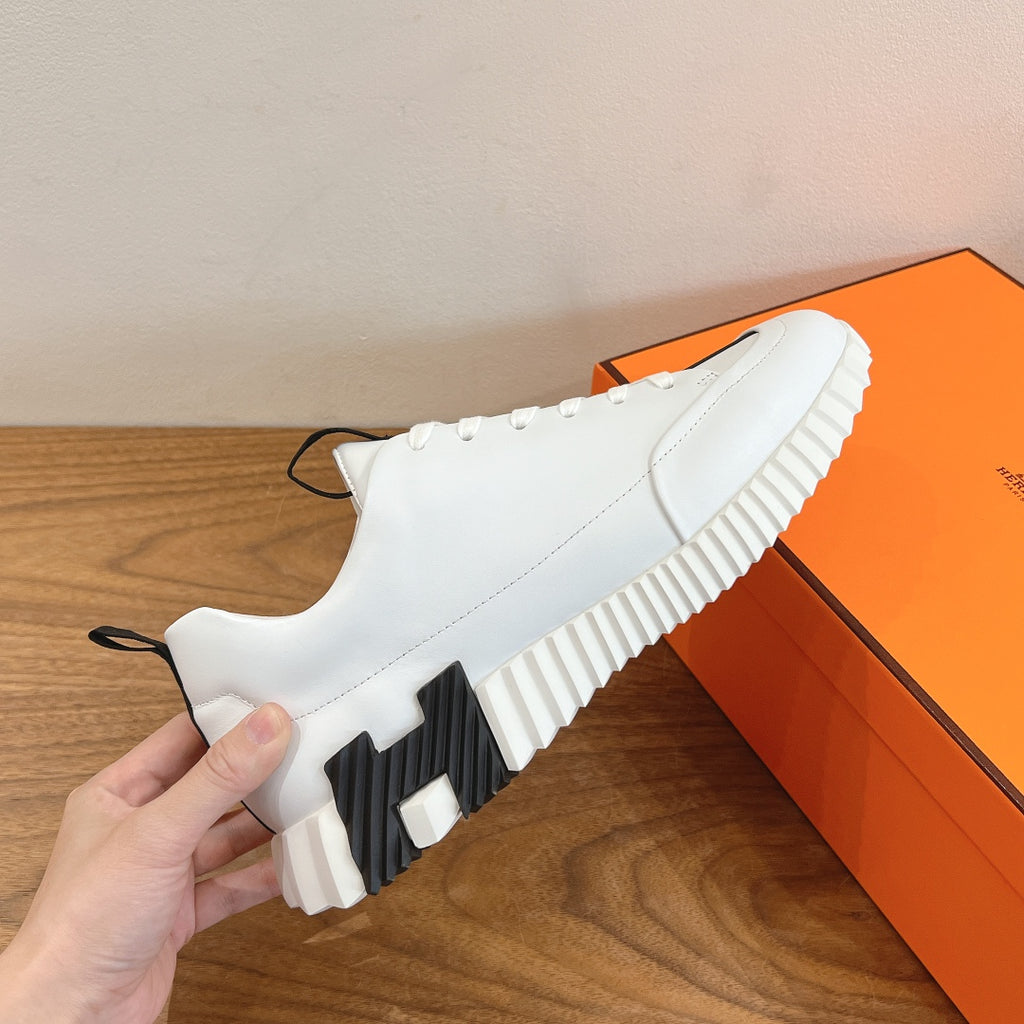 White sneaker side view with ribbed platform sole and black accent panel, Hermes.