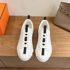White sneakers with black side stripe, lace-up front, Hermes unisex design.