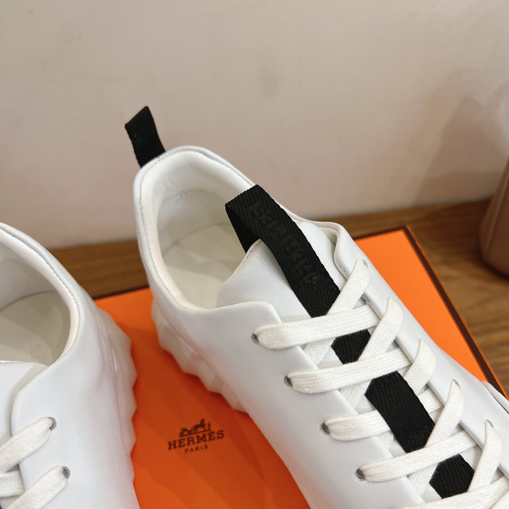 White sneaker tongue and laces with black strap, Hermes branding inside.