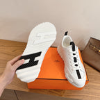White sneaker outsole and side view with black tread accents, Hermes unisex.