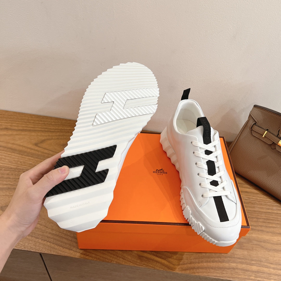 White sneaker outsole and side view with black tread accents, Hermes unisex.