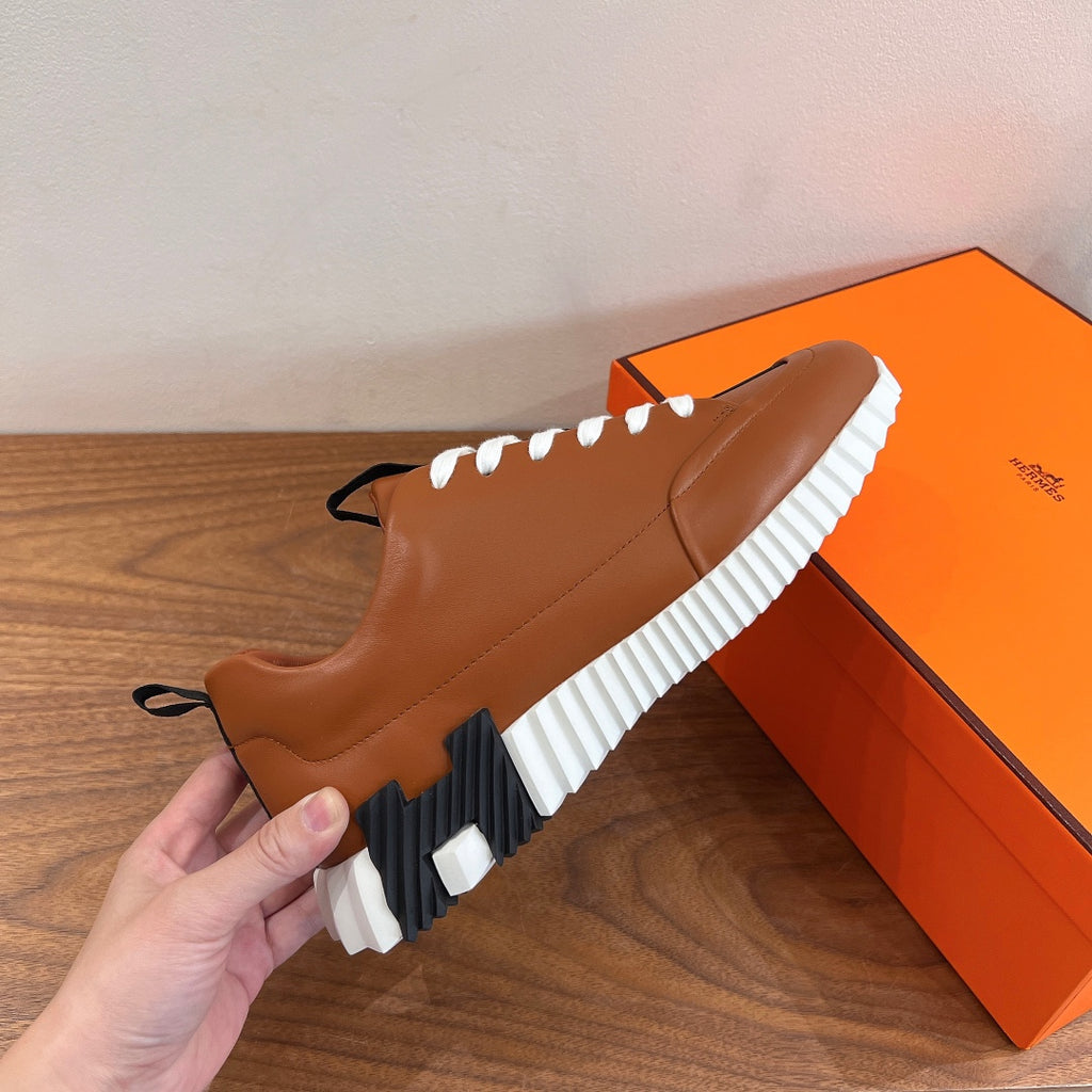 Tan leather sneakers with white laces and striped rubber sole, held in hand