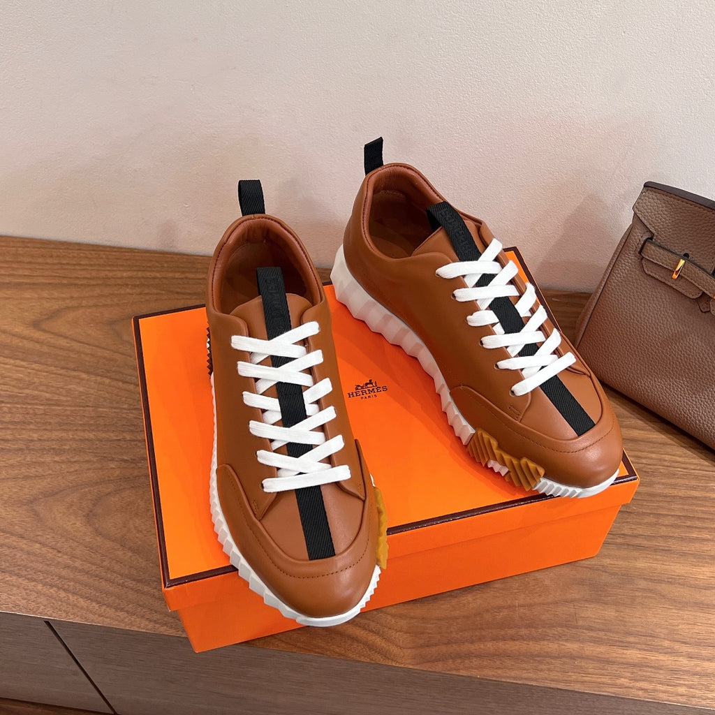 Tan leather lace-up sneakers with black side stripe displayed on orange box