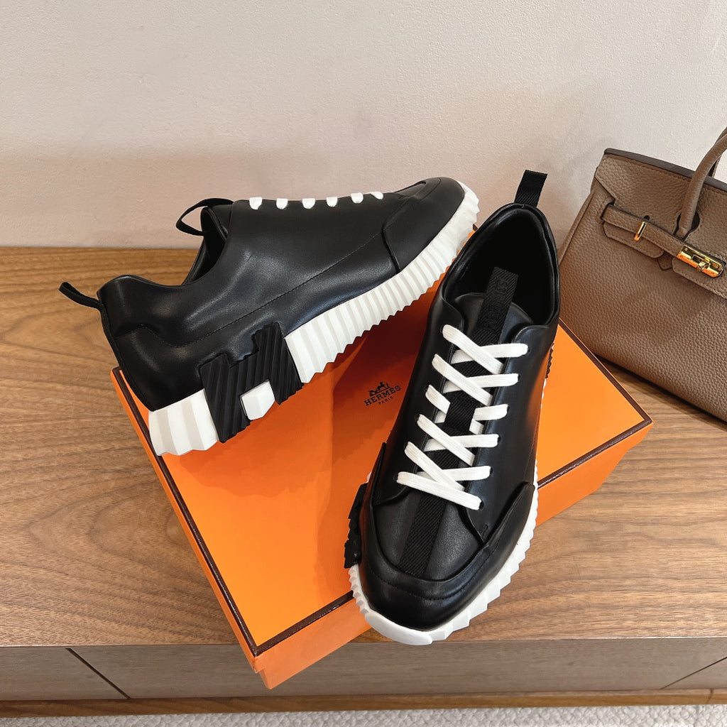 Black sneakers with white laces, chunky sole, and elastic side pull tabs