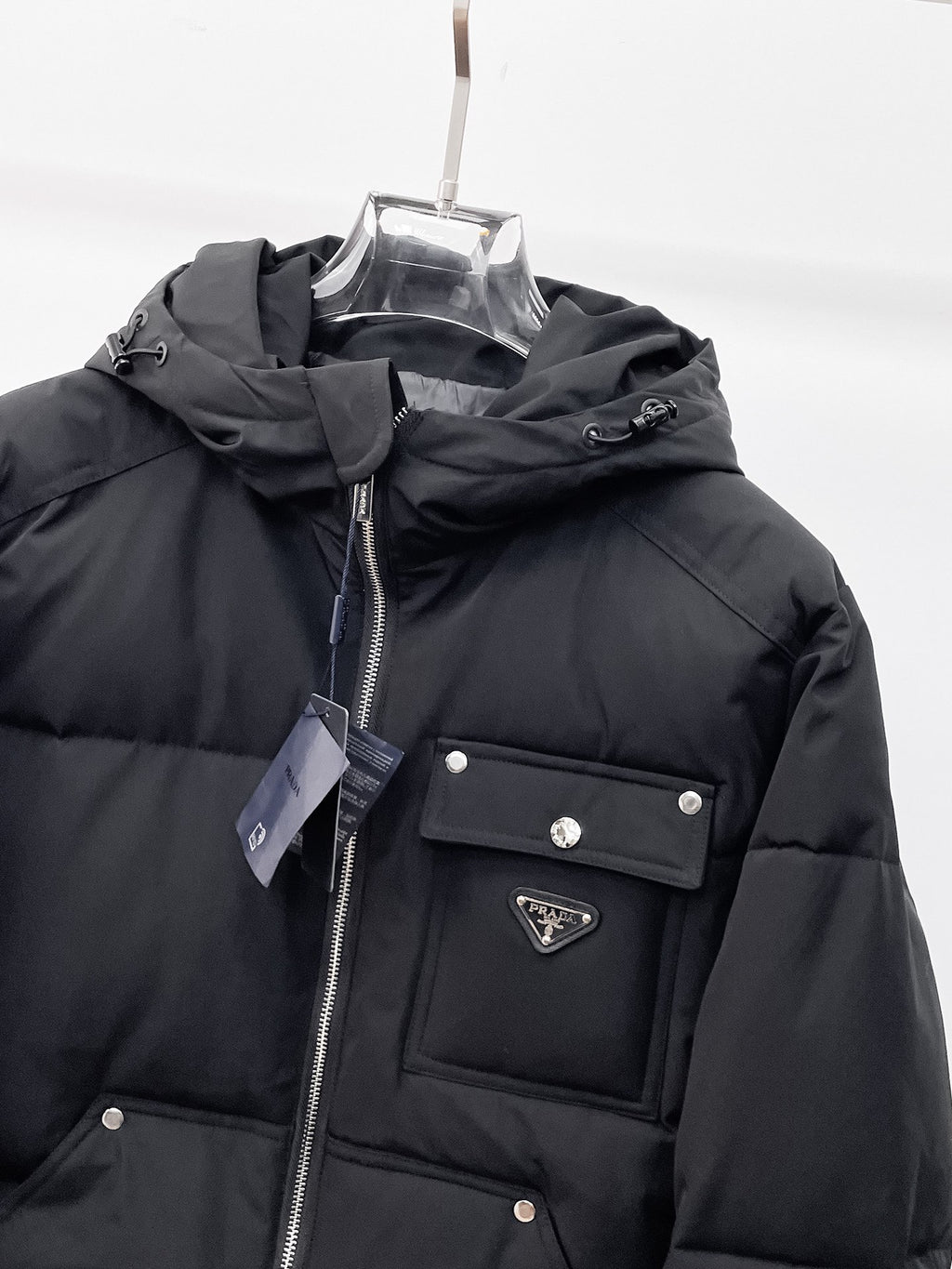 Black hooded puffer jacket front close-up with zipper, logo patch, and flap chest pocket