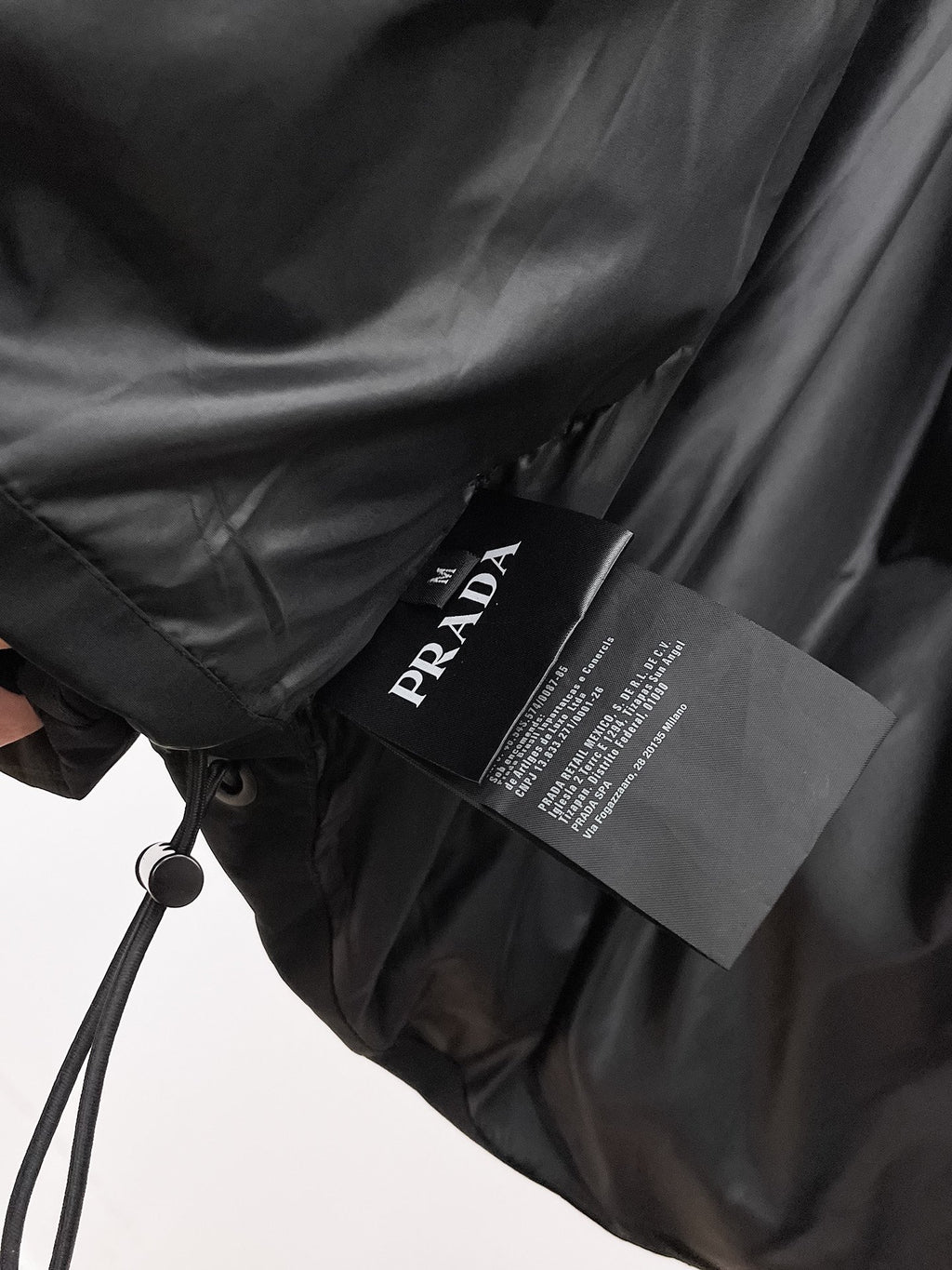 Long black coat with drawstring waist and Prada branded hang tag
