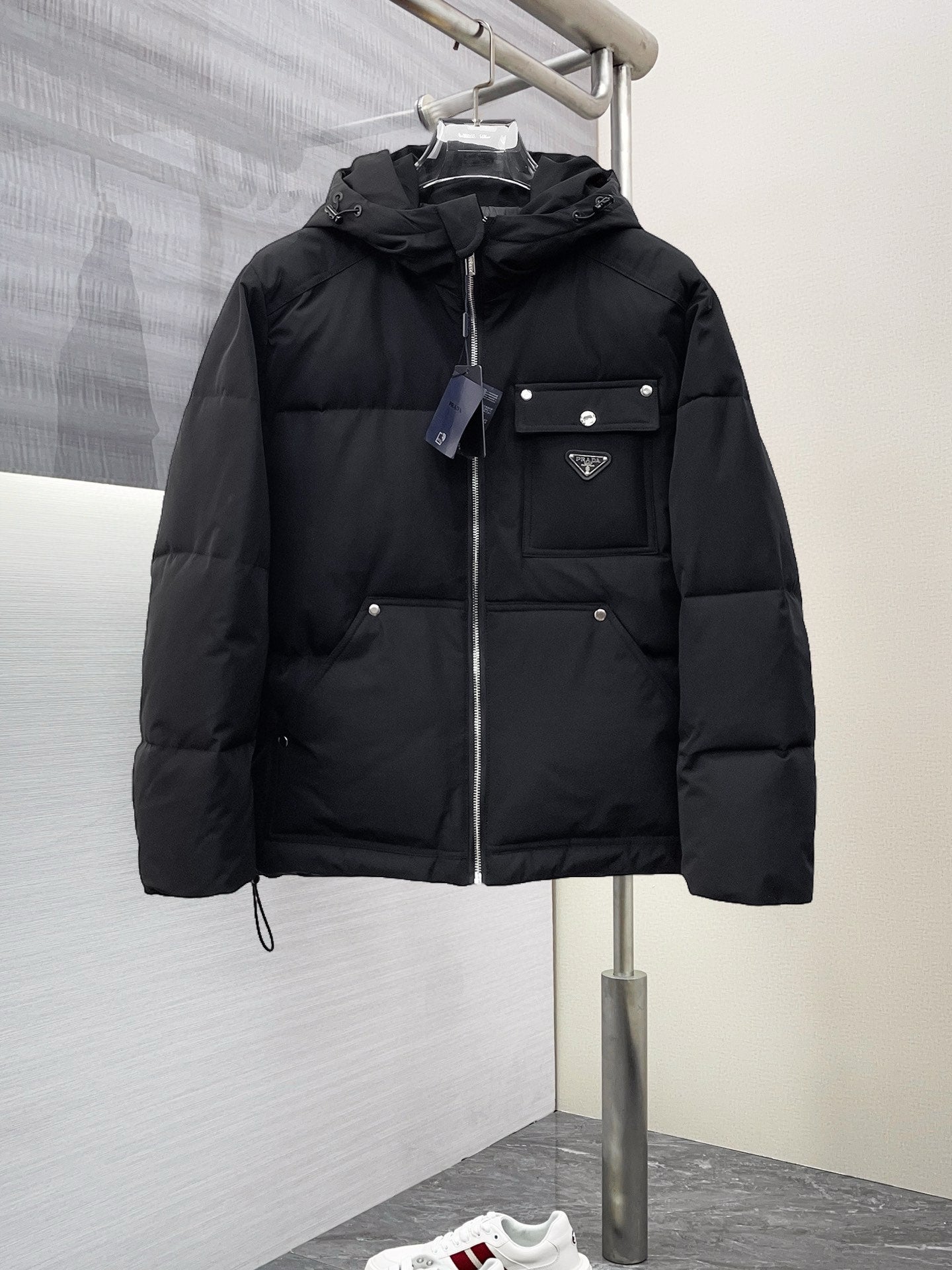 Black long puffer jacket with hood, full zipper, and front flap pockets