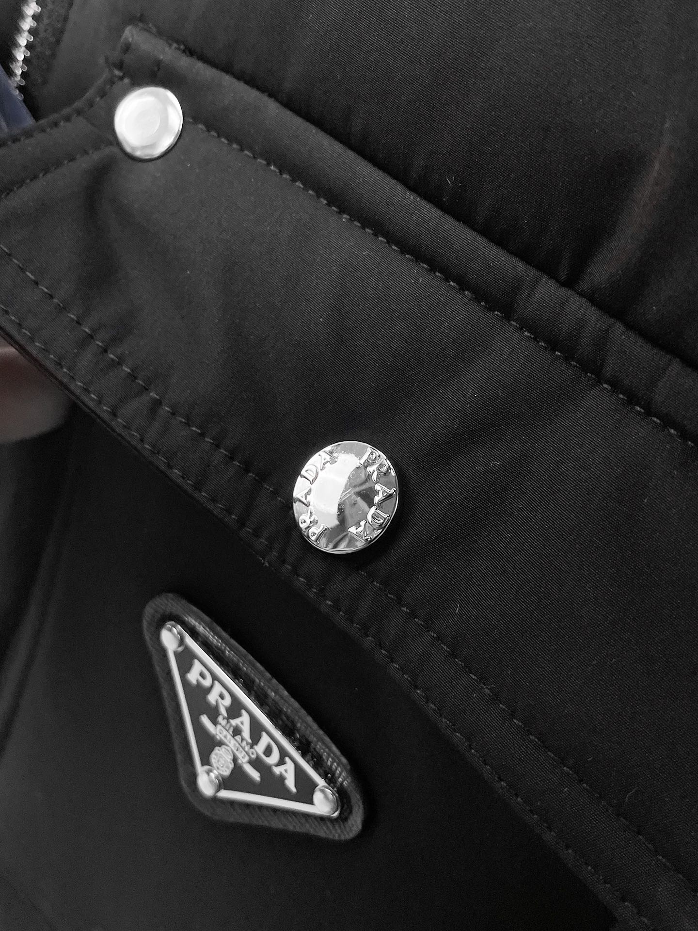 Black puffer jacket close-up of snap buttons and fabric logo patch on pocket