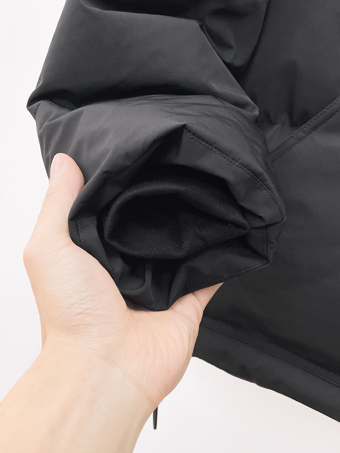 Black puffer jacket sleeve close-up held in hand, showing cuff and quilted stitching
