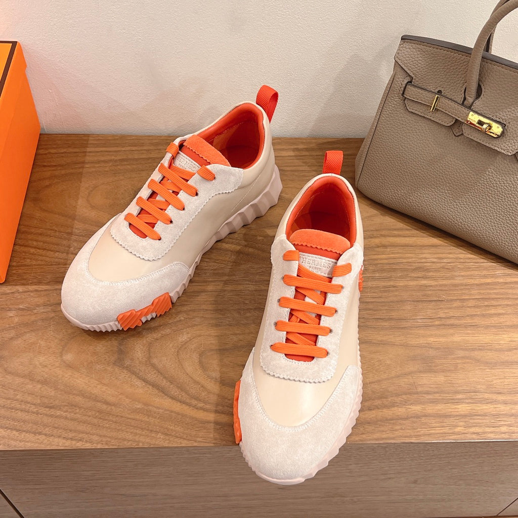 White and orange Hermes-style sneakers with lace-up closure and textured rubber sole.
