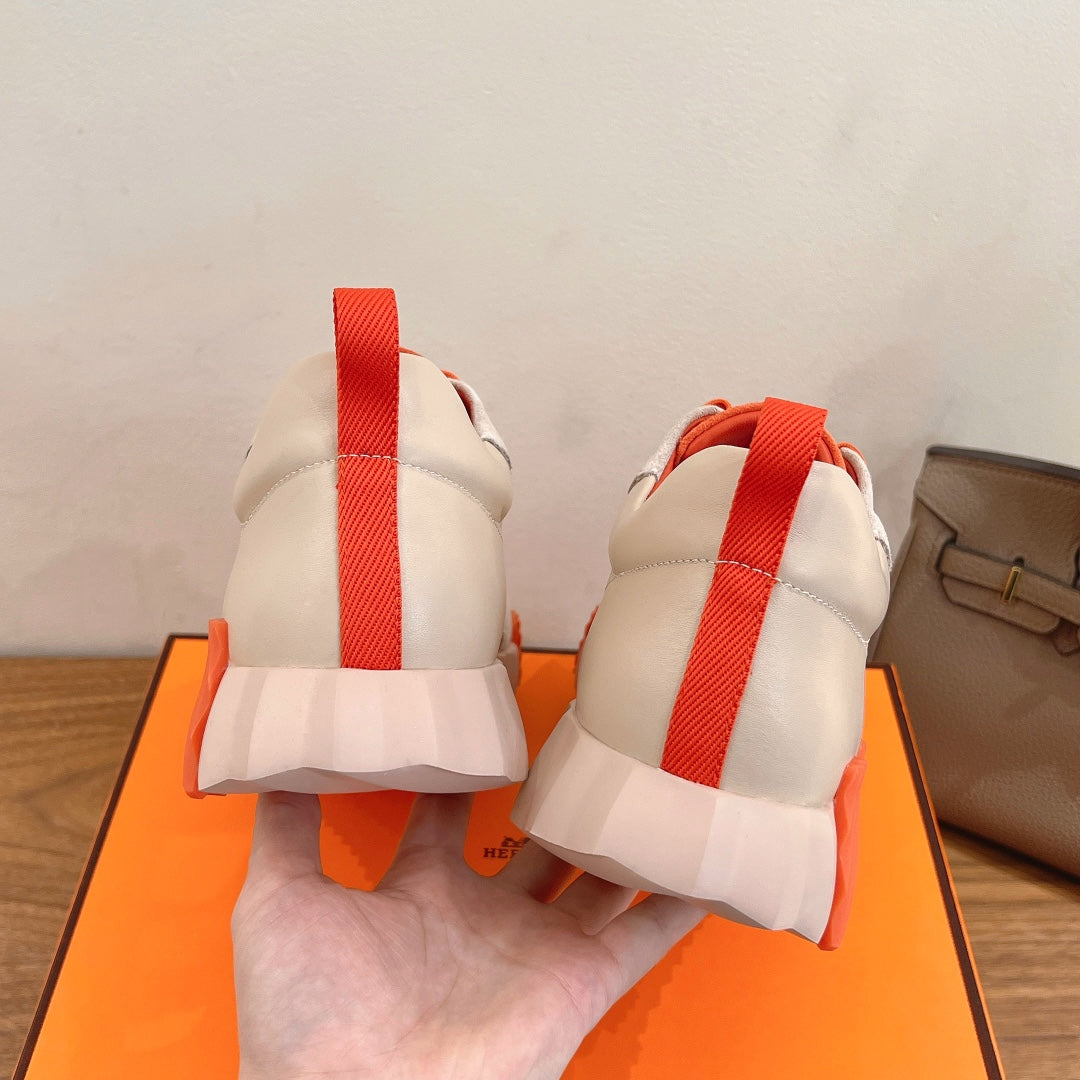 Rear view of white sneakers with orange heel tab strap and cushioned back collar.