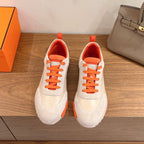 White and orange sneakers with orange laces and thick rubber sole, unisex style.