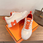 White and orange sneakers posed on an orange box, showing lace-up front and sole.