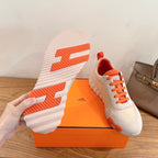 Sneaker outsole and side view: white tread with orange H-like motif.