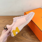 Hermes pink low-top sneakers, hand-held view with yellow accent on striped sole