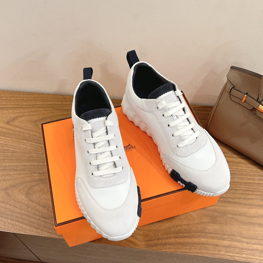 Hermes unisex sneakers with white uppers, navy heel tabs, and lace closure.