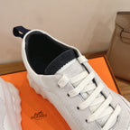 White Hermes sneakers with navy collar lining, lace-up front, and stitched toe.