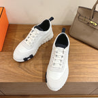 White lace-up Hermes sneakers with navy heel lining and textured rubber sole.