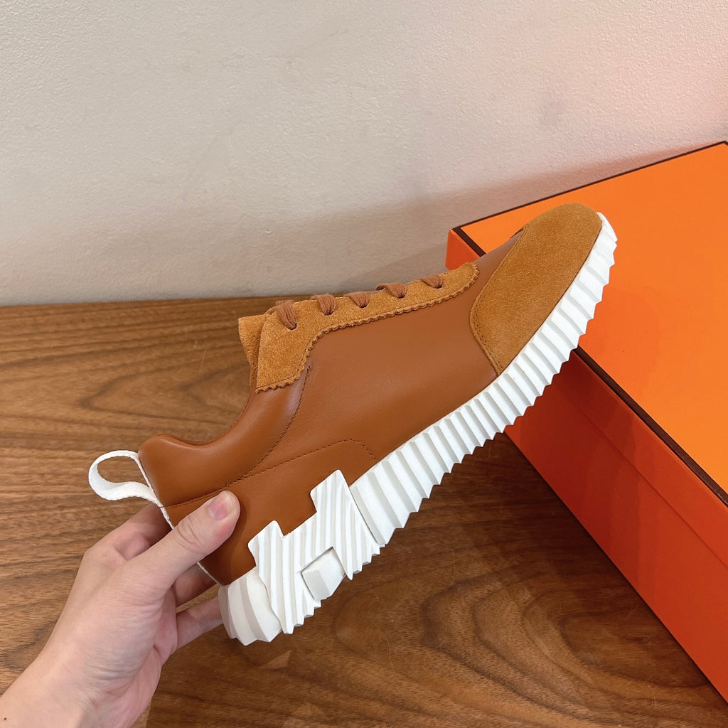 Tan sneakers with lace-up upper and thick white ridged sole, held up
