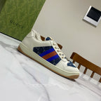 Gucci unisex low-top sneakers angled side view, white upper with blue panel and rainbow web stripe