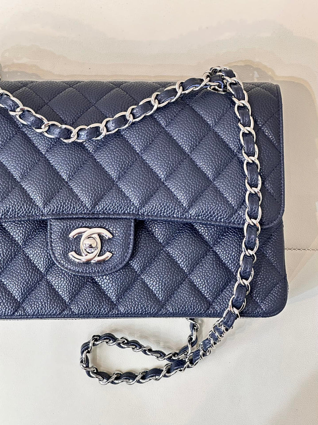 Quilted navy leather flap bag detail view with chain strap and Chanel logo button.