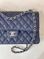Quilted navy leather flap bag detail view with chain strap and Chanel logo button.