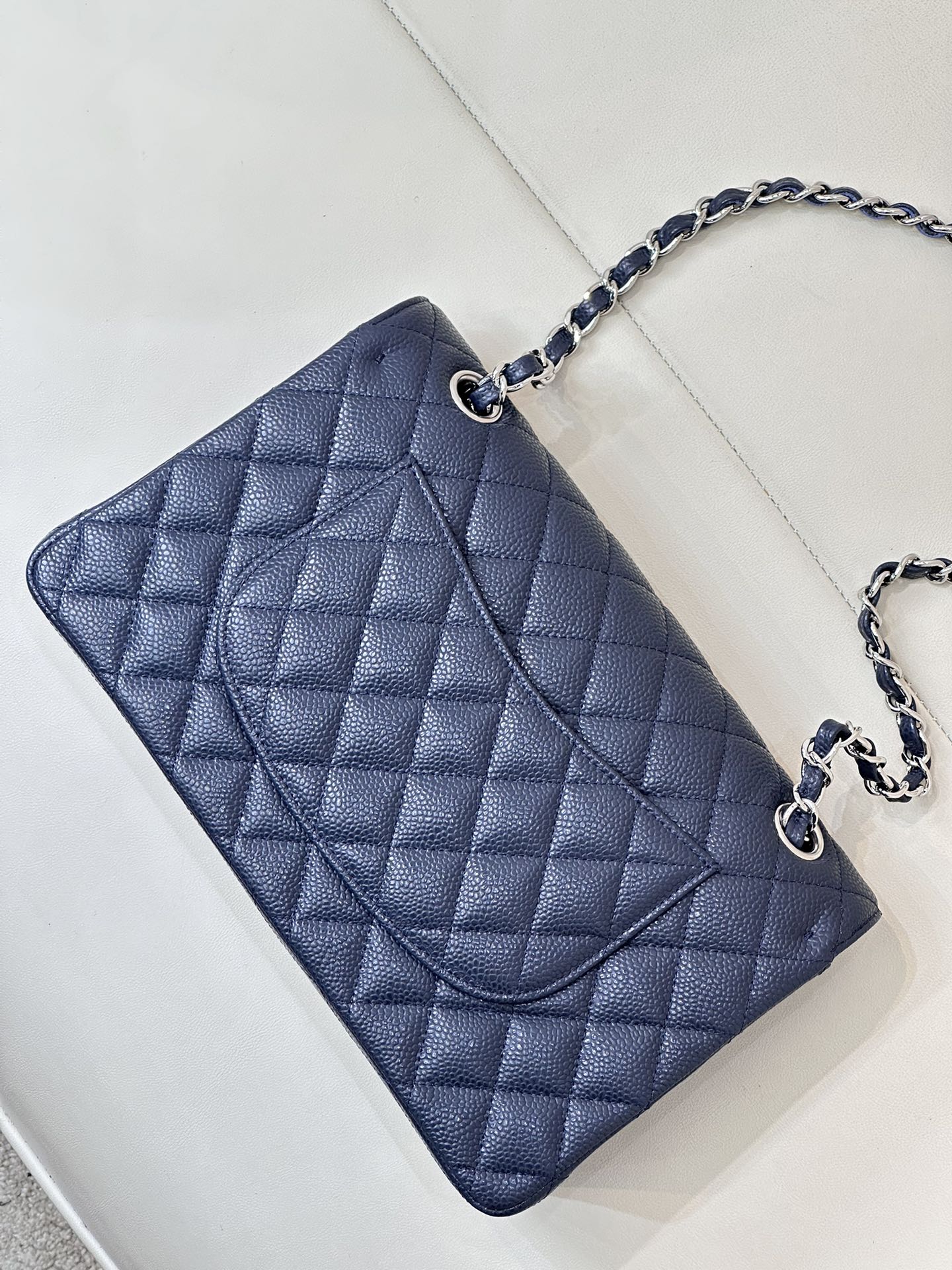 Quilted leather flap shoulder bag with chain strap, angled top view, dark navy blue.
