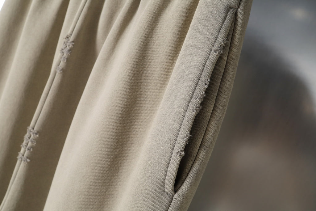 Beige pants with side seam detail and small distressed patches on fabric.