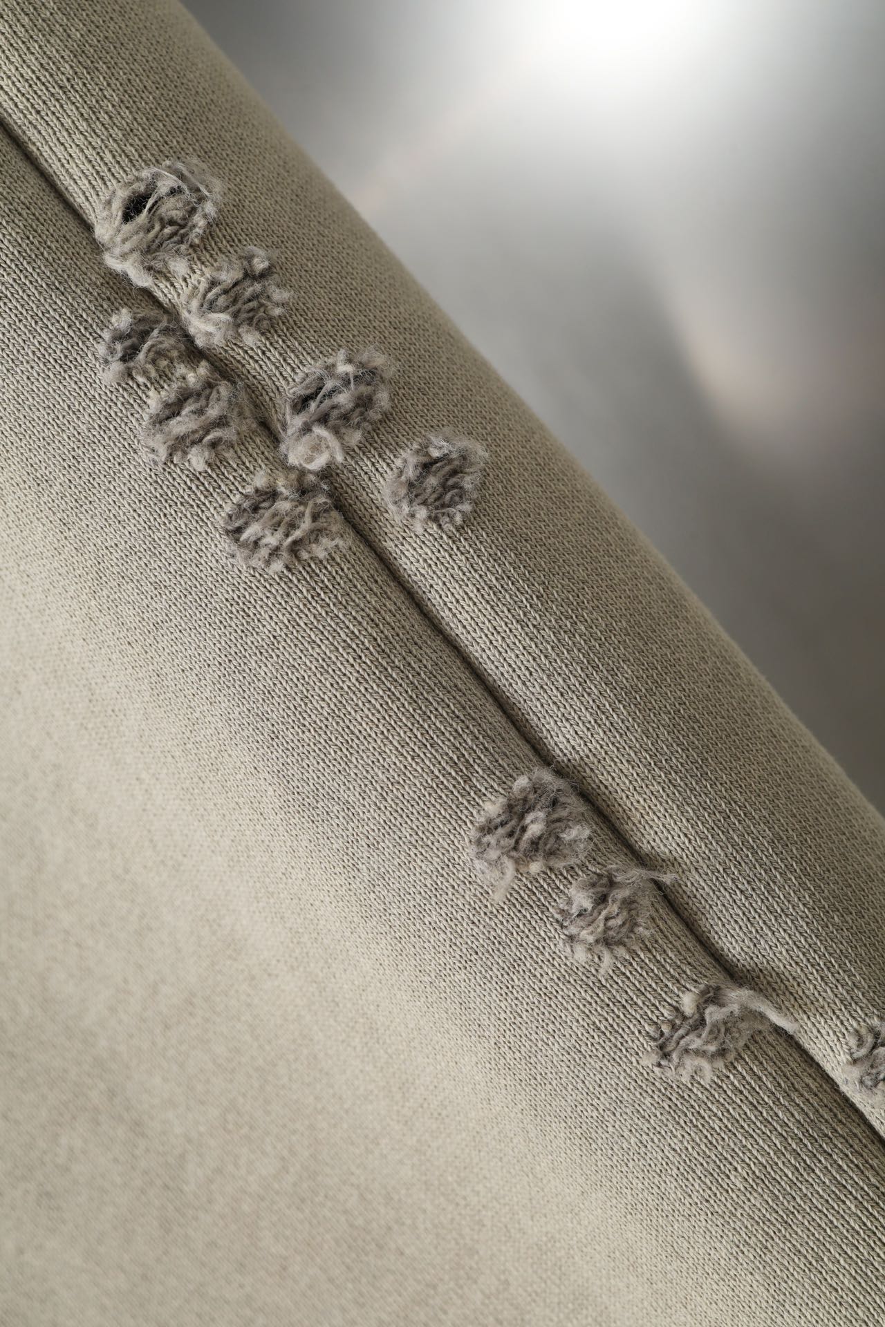 Beige pants cuff with frayed distressed trim along the hem.