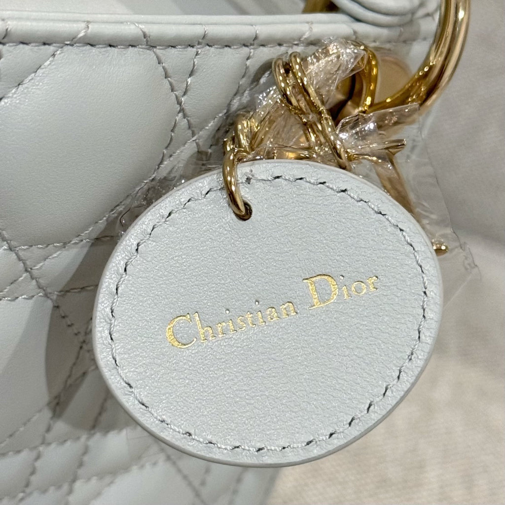 Dior bag close-up: round "Christian Dior" tag charm on white quilted leather