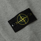 Stone Island black logo patch with yellow emblem on gray knit sweater sleeve