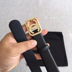 Dark leather belt with gold square logo buckle and rhinestone border, held in hand over pouch.