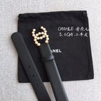 Black leather belt with faux pearl logo charm and side row of punched holes.