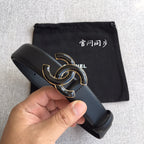 Dark leather belt with gold-tone interlocking C buckle held in hand with dust bag.