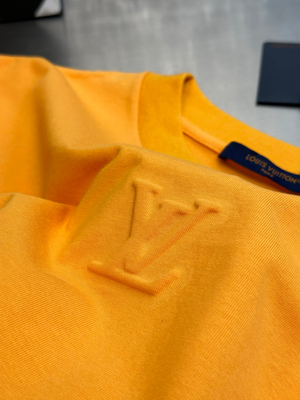 Louis Vuitton yellow T-shirt with raised LV emblem on chest, studio close-up
