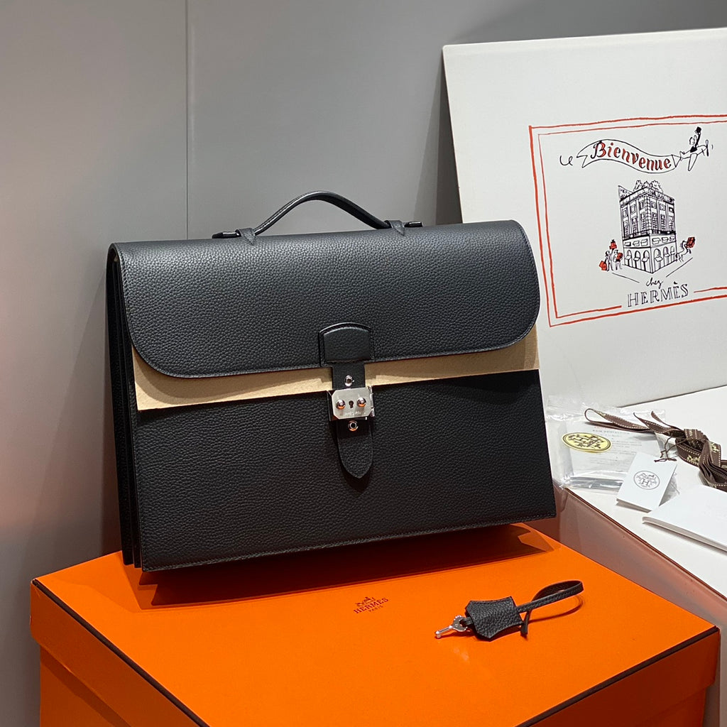 Hermes bag in dark leather with top handle, front flap, and metal lock clasp.