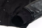 Ribbed cuff and snap placket on black varsity jacket with leather-look sleeve