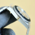 Rolex watch side profile with ribbed bezel, crown, and steel bracelet, brushed finish