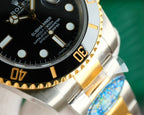 Rolex watch bezel close-up with gold indices and two-tone metal bracelet links