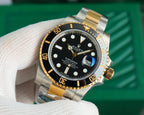 Rolex watch front view with black dial, gold bezel accents, and two-tone metal bracelet