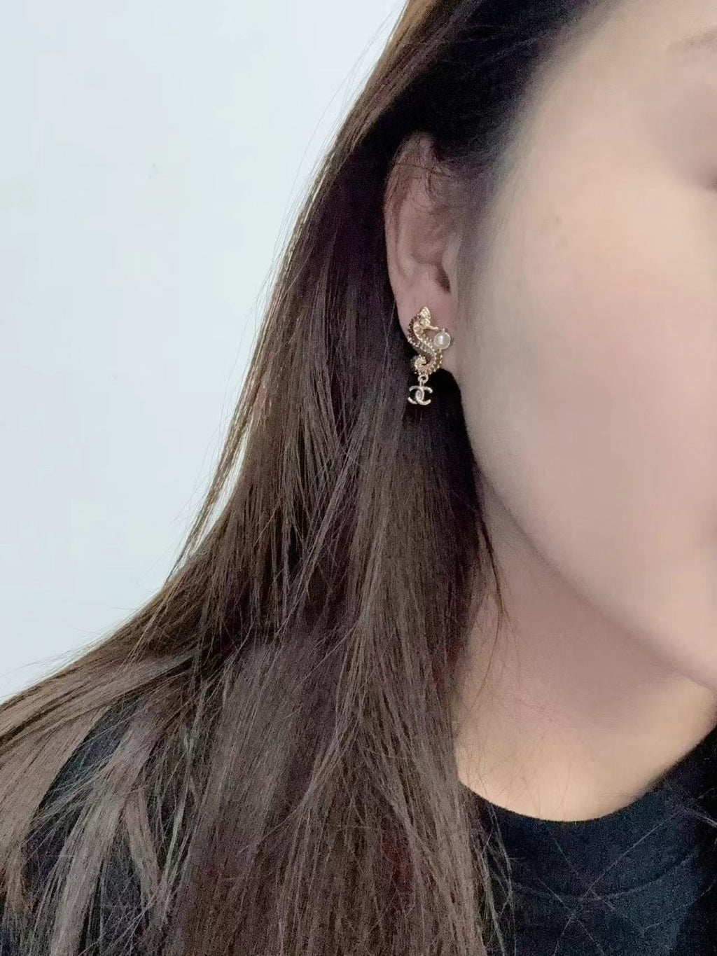 Gold-tone Chanel CC dangle earrings with pearl accents, worn on ear side view