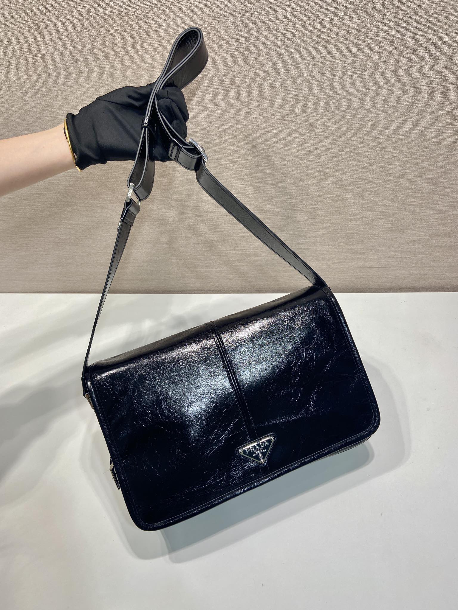 Dark leather crossbody bag with long strap and front flap with triangle emblem