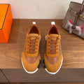 Hermes unisex sneakers in tan suede with orange laces and white sole, side view