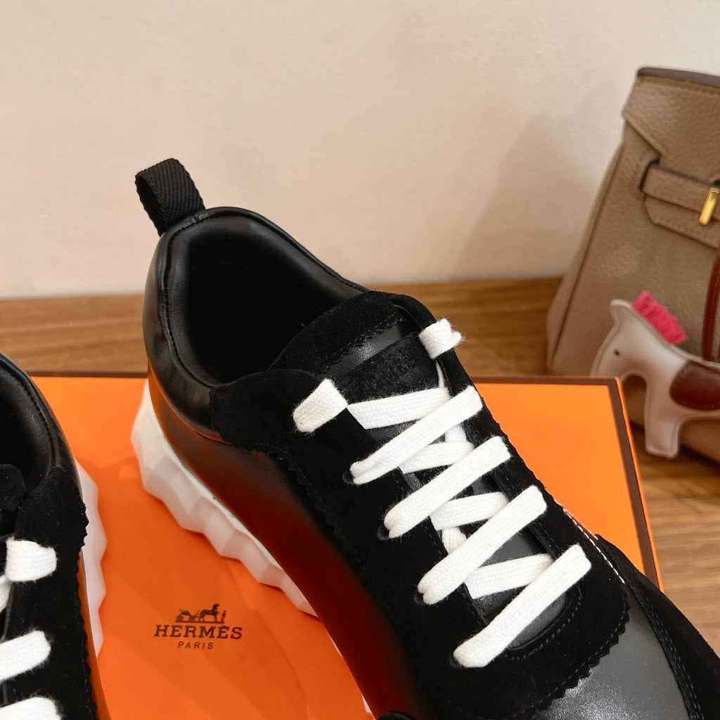 Close-up of black Hermes unisex sneaker with white lace stitching and glossy front panel