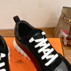 Close-up of black Hermes unisex sneaker with white lace stitching and glossy front panel