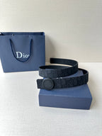 Dior belt with dark monogram strap and round gray buckle beside blue gift box